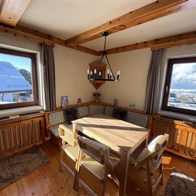 Un coin repas confortable avec un revêtement en bois et une table au centre. Les fenêtres offrent une vue sur le paysage montagneux.