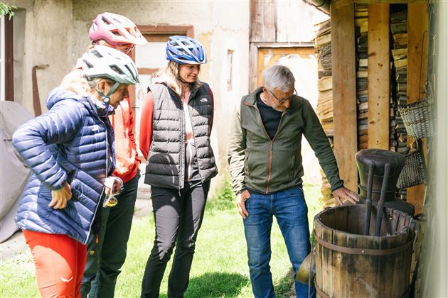 A group of four people is curiously looking at a wooden barrel outdoors. They are wearing bicycle helmets and casual clothing to feel comfortable.