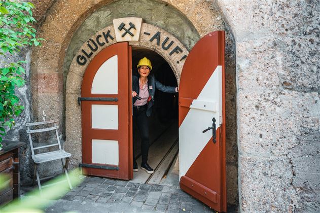 Un homme se tient devant une grande porte ouverte avec l'inscription « Bonne chance! ». Il porte un casque et regarde dans un étroit tunnel.