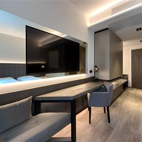 A modern room with a large television and a desk. The decor is stylish and minimalist, featuring bright colors and a hardwood floor.