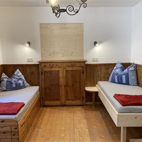 A cozy room with two single beds and rustic wooden furniture. The walls are in warm tones, and there are beautiful cushions on the beds.