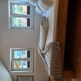 Ein gemütliches Schlafzimmer mit einem großen Bett und zwei Fenstern. Das Zimmer hat helle Wände und einen warmen Holzboden.