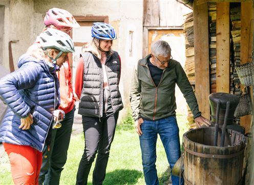 Eine Gruppe von vier Personen betrachtet interessiert ein Holzfass im Freien. Sie tragen Fahrradhelme und lässige Kleidung, um sich wohlzufühlen.