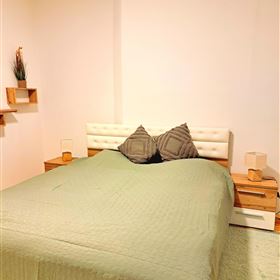 A cozy bedroom with a large bed and simple nightstands. The walls are light and the floor is carpeted.