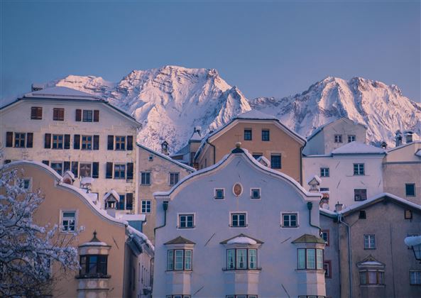 Eine malerische winterliche Stadtansicht mit schneebedeckten Häusern. Im Hintergrund erheben sich majestätische Berge.