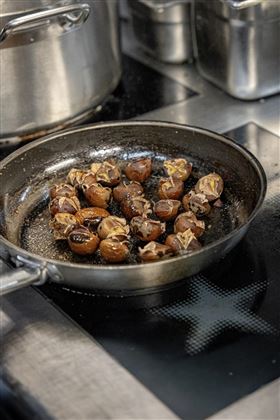 Castagne arrosto in una padella sul fuoco. Lo sfondo mostra utensili da cucina e una cucina moderna.