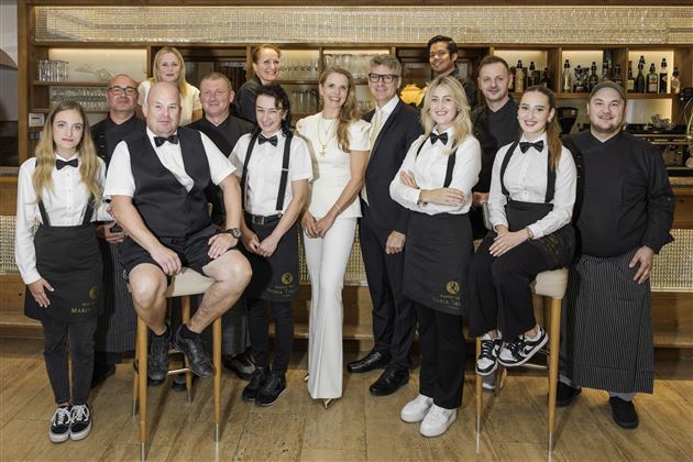 Un gruppo di dipendenti in abbigliamento formale si trova in un ristorante. Sorridono gentilmente e posano per la foto.