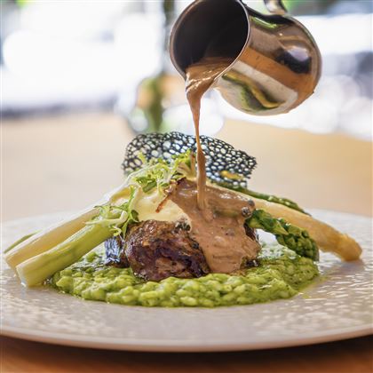 Un piatto elegante su un piatto, composto da risotto verde, carne tenera e verdure. Una salsa viene versata sopra il cibo, creando un punto culminante visivo.