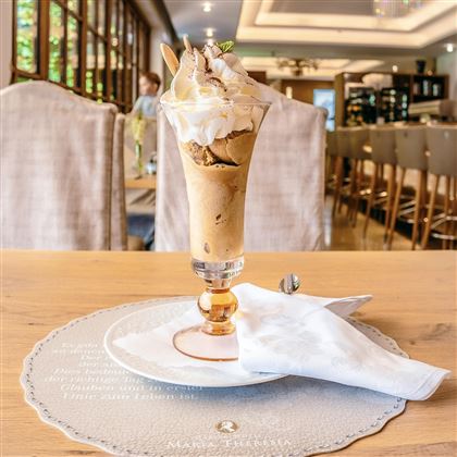 Un delizioso dessert di gelato in un elegante bicchiere, guarnito con panna e una piccola decorazione. Sullo sfondo si possono vedere mobili stilosi e un'atmosfera accogliente.