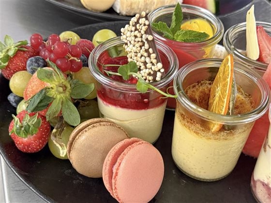 Un vassoio con diversi dessert in bicchieri e frutti colorati. Ci sono macarons, bacche e una decorazione decorativa.