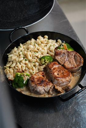 Un piatto delizioso con carne succulenta, contorni di pasta e broccoli freschi. Il piatto è presentato in modo accattivante e ha una salsa cremosa.