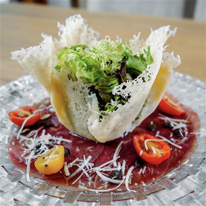 Un piatto artisticamente impiattato con una porzione di insalata in una ciotola croccante. Circondato da fette di pomodoro e formaggio, il piatto appare fresco e appetitoso.