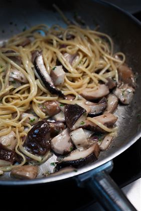Un piatto con spaghetti e funghi in una padella. La pasta è leggermente guarnita con una salsa alle erbe.