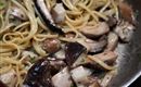 Un piatto con spaghetti e funghi in una padella. La pasta è leggermente guarnita con una salsa alle erbe.