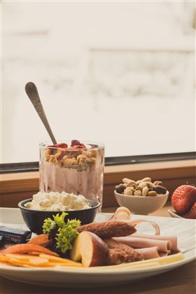 Un tavolo con una deliziosa colazione. La colazione comprende yogurt con frutta, formaggio, prosciutto e verdure fresche.