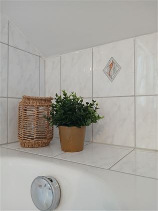 A stylish bathroom corner with a plant in a pot and a decorative basket. The walls are adorned with white tiles.