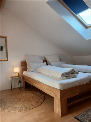 A cozy bedroom with two single beds and a wooden frame. A window with natural light and a small lamp create an inviting atmosphere.