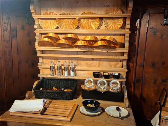 A rustic wooden shelf with various bowls and spice containers. Below are snacks in a basket and a small bowl.