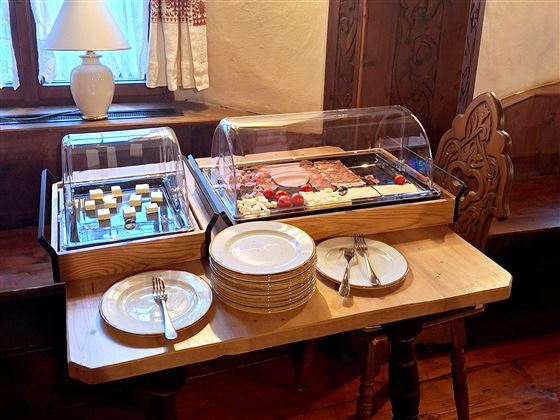 A table with two glass boxes full of delicious snacks, including cheese and sausage. Beneath, several plates and cutlery are ready.
