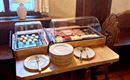 A table with two glass boxes full of delicious snacks, including cheese and sausage. Beneath, several plates and cutlery are ready.