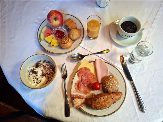 A hearty breakfast with various rolls, cold cuts, cheese, and fruit. Accompanied by coffee and juices on a table.