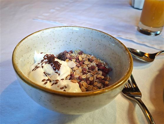 A bowl of muesli, yogurt, and chocolate chips. In the background, a glass of juice is visible.