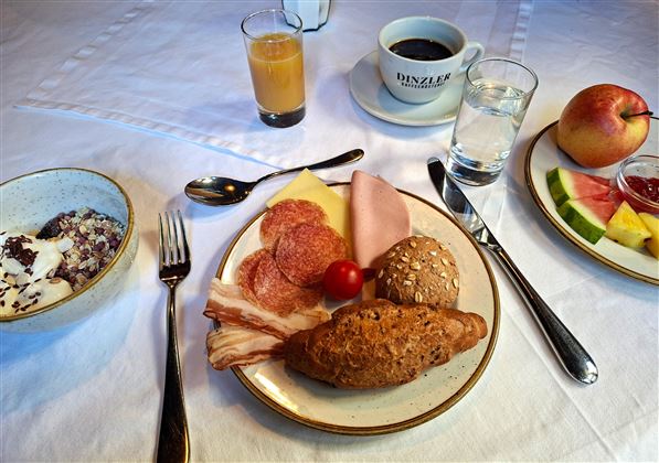 A hearty breakfast with various types of sausage, cheese, fresh fruit, and rolls. Coffee and juices are on the table.