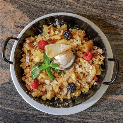 Un delizioso dessert in una ciotola, composto da ingredienti croccanti, frutti di bosco e una pallina di gelato. La menta fresca aggiunge una nota speciale al piatto.