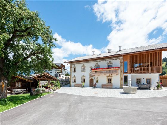 A beautiful traditional building with wooden siding and a large tree in the foreground. The sky is clear and blue, and the surroundings seem calm and inviting.