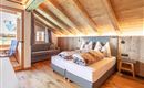 A cozy bedroom with wooden walls and a sloped ceiling. There is a double bed, a sofa, and large windows that let in a lot of light.