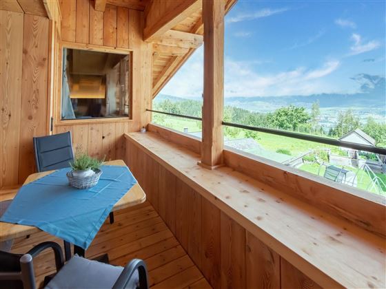 A cozy balcony with wooden cladding and a view of a green landscape. The table is decorated with a blue tablecloth and a plant.