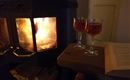 Een gezellige open haard met een warm vuur. Twee glazen met een drankje staan op een tafel naast een boek.