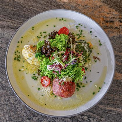 Un bel piatto con insalata fresca, erbe colorate e una polpetta di carne. Il piatto è presentato in modo attraente e appare molto invitante.