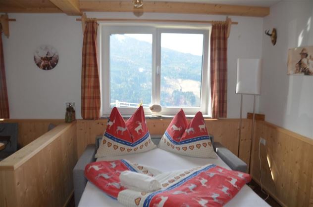Een gezellige slaapkamer met een groot raam en uitzicht op de bergen. Het beddengoed is kleurrijk en typisch alpenlands versierd.