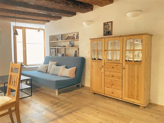 A cozy living room with a blue sofa bed and a wooden cabinet. Large windows provide plenty of daylight.