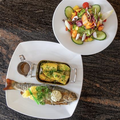 Un piatto con pesce fritto, accompagnato da una porzione di patate e una ciotola di insalata fresca. Il piatto è preparato con cura e ricco di colori.