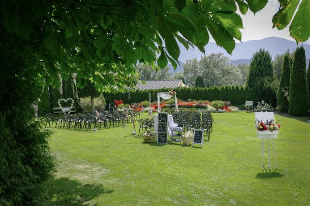 Un bel giardino con sedie per un evento. Sullo sfondo si possono vedere numerosi fiori e alberi.
