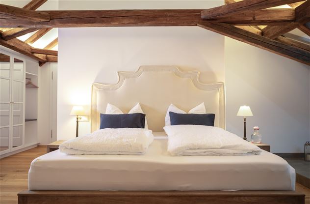 A modern bedroom with a large, comfortable bed and elegant pillows. The wooden ceiling and soft lighting create a cozy atmosphere.