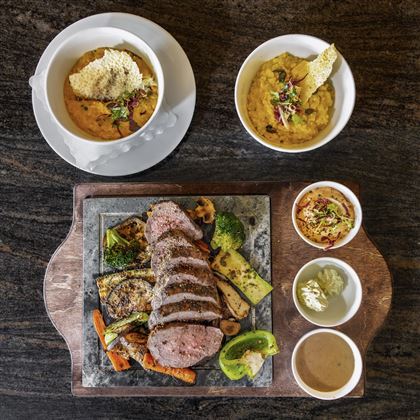 Un delizioso piatto con carne tenera e verdure colorate, servito su un tagliere di legno. Accanto al piatto principale ci sono due ciotole con diversi contorni.