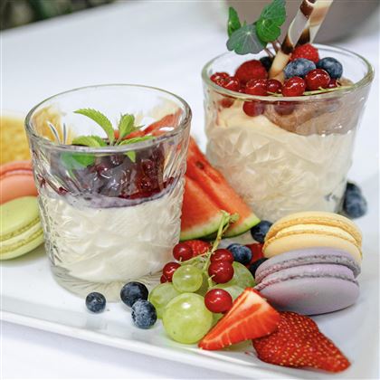 Due deliziosi dessert in bicchieri, circondati da frutta fresca e macarons. La disposizione colorata rende il tutto appetitoso e invitante.