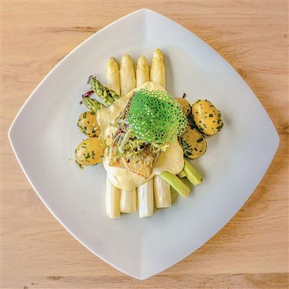 Un piatto artisticamente presentato con asparagi, patate e una salsa cremosa. Il piatto è guarnito con erbe fresche e appare appetitoso.