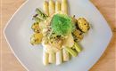 Un piatto artisticamente presentato con asparagi, patate e una salsa cremosa. Il piatto è guarnito con erbe fresche e appare appetitoso.