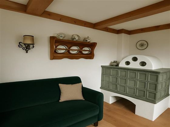 Un salon confortable avec un canapé vert et un poêle au design traditionnel. Des éléments décoratifs et des miroirs sont accrochés au mur.