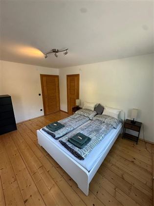 Una camera da letto luminosa con un grande letto matrimoniale e due comodini. Il pavimento è in legno e c'è un armadio nell'angolo.