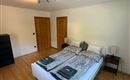 Una camera da letto luminosa con un grande letto matrimoniale e due comodini. Il pavimento è in legno e c'è un armadio nell'angolo.