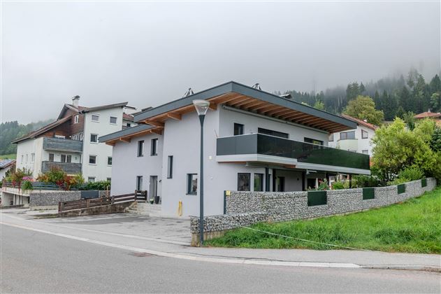 A modern house with a bright exterior paint and large windows. It is located in a quiet area, surrounded by green countryside.
