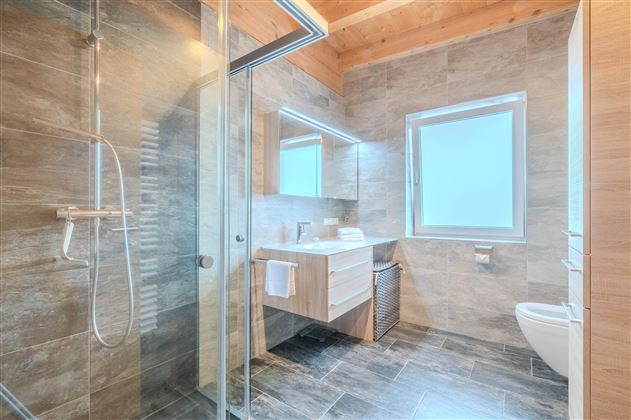A modern bathroom with a large shower and elegant wood details. The sanitary facilities are clearly structured and offer plenty of natural light.