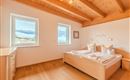 A bright bedroom with a wooden ceiling and large windows. The view of the mountains and the lake creates a relaxing atmosphere.