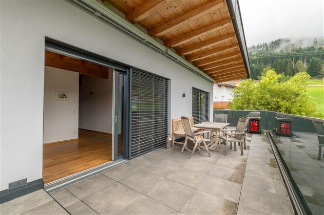 A modern terrace with a table and chairs. In the background, green meadows and a cloudy sky can be seen.