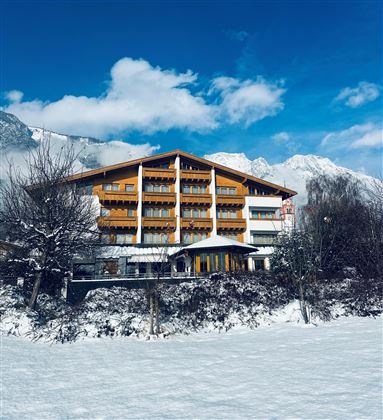 A cozy hotel in the mountains with several floors. The surroundings are snow-covered and the mountains are visible in the background.